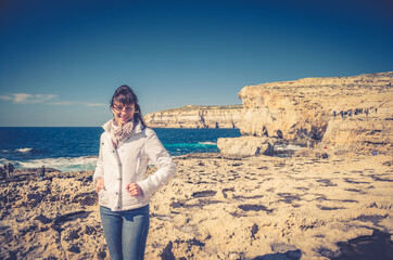 Young woman traveler with white jacket and headscarf looking at camera and smile on stone rocks of...