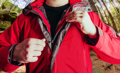 Fototapeta na wymiar Photo of a male person putting on red travel hiking jacket in summer woods background.