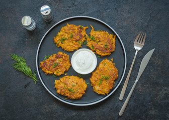 Sweet potato or carrot fritters on a black plate on a dark concrete background. Vegetarian recipes.