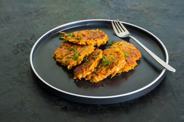 Sweet potato or carrot fritters on a black plate on a dark concrete background. Vegetarian recipes.