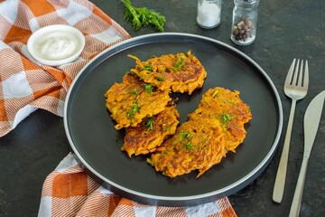 Sweet potato or carrot fritters on a black plate on a dark concrete background. Vegetarian recipes.