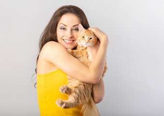 Happy young fun woman holding on the hands her red maine coon kitten. Closeup portrait