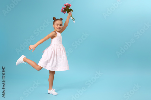 happy little girl holds bouquet of roses and runs isolated on blue studio background. Mother's day.