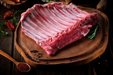 Raw lamb meat on the bone in a large whole piece, organic halal lamb with seasonings on a wooden...