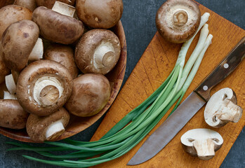 Champignon mushrooms in a wooden bowl and green onions, close-up, top view, shallow depth of field