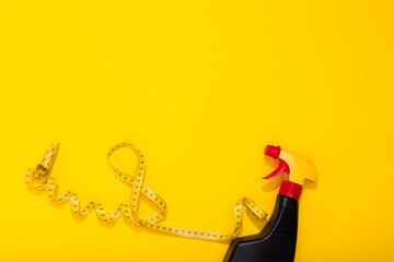 A black bottle with chemical spray and centimeter tape in eight shape on yellow background with copy space, text place. Cleaning agent. Woman day. Holiday gift certificate. Cleaning service. Mockup