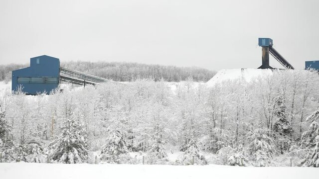Slow motion passing snow covered landscape with coal mine elevators surrounded by forest in the winter.