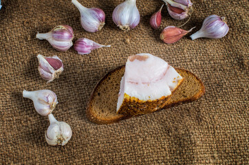 heads of garlic slice of black bread a piece of lard on burlap. Rustic style