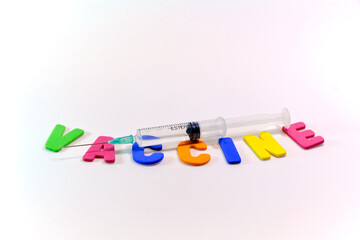 Syringe on a white background and with the word vaccine with colored letters.