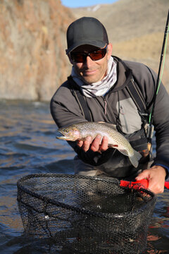 happy modern fly fisherman holding fresh-caught cutthroat trout