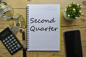 Flat lay of calculator, coin, pen, smart phone, plant and notebook written with " Second Quarter ". Business, financial and education concept. Selective focus.