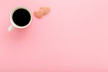 White cup of black coffee and heart shapes of dry cookies on light pink table. Pastel color. Empty...