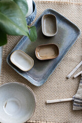 Three pretty ceramic trays over a greater one on a brown tablecloth next to some kitchenware utensils.