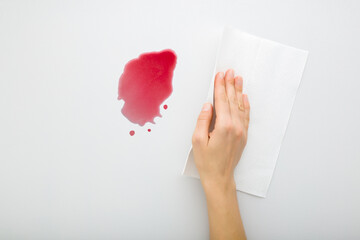 Young adult woman hand cleaning fresh spilled red beverage from light gray table background. Wine...