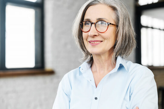 Headshot Portrait Of A Charming Smiling Elegant Senior Woman In Glasses Standing And Looking Away, Thinking Of The Bright Company Future. Close-up Of A Middle-aged Gray-haired Female Business Owner