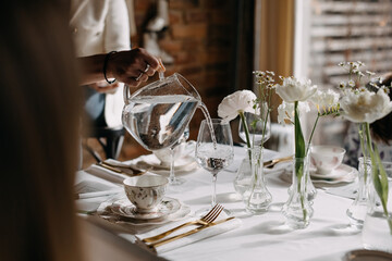 Woman pouring water from a transparent jug into a glass at a restaurant.