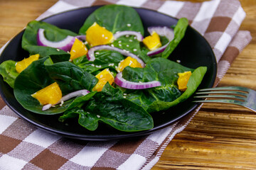 Tasty salad with spinach, orange, red onion and sesame seeds on wooden table. Healthy food or vegetarian concept
