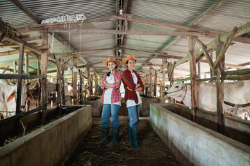 Obraz na płótnie Canvas Two cattle breeders wearing casual clothes and hats stand back to back and pose crossed hands in the cattle breeding pen
