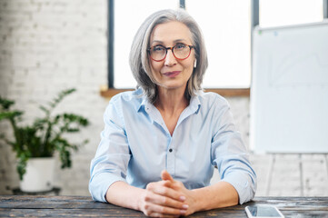 Serious intelligent mature senior teacher businesswoman with pleasant smile and earphones in...
