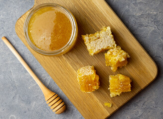 Top view of jar with honey and honeycomb on wooden board on cement surface