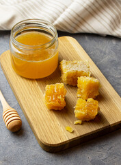 Honeycomb and jar of fresh honey on wooden board with wooden honey spoon on concrete surface