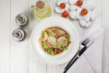 Caesar salad with herbs and meat on a white wooden table
