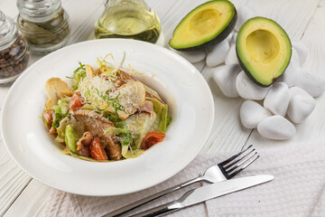 Caesar salad with herbs and meat on a white wooden table
