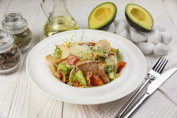 Caesar salad with herbs and meat on a white wooden table
