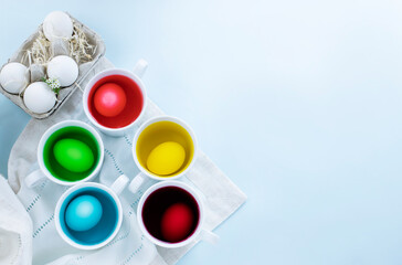 Close up of easter eggs dye process and eggs in carton against light blue background. Image with copy space