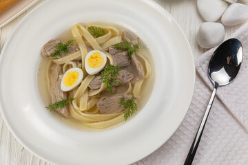 Broth with veal, eggs, noodles on a white wooden table
