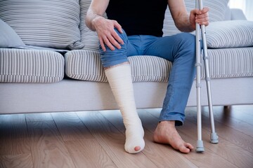 Man with broken leg at home. Leg in plaster. He holds the crutches in his hand.