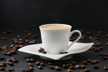 Coffee beans on a black table. White cup of coffee on a black background. Close-up side view.