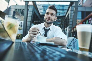 Businessman in cafe terrace outdoors in front of office building, wide and low angle view.