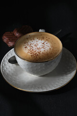 White cup of cappuccino on a black table. Italian cappuccino. Morning coffee. Chocolate chip cookies. Morning dessert in the sun. Italian breakfast. Black textured table.