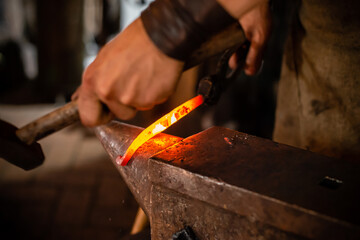 A blacksmith forging horseshoe with hammer. blacksmith forges a horseshoe in a forge on an anvil A forging furnace with fire at the background.