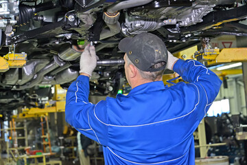 A worker attaches the part to the underside of the car. Assembly line of an automobile plant - 415643070