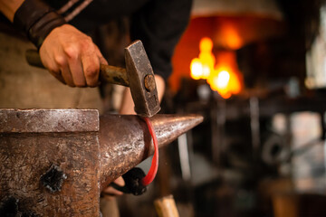 A blacksmith forging horseshoe with hammer. blacksmith forges a horseshoe in a forge on an anvil A forging furnace with fire at the background.