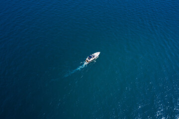 Obraz premium Lonely boat on blue water. White yacht slow motion on blue water, boat top view. Boat in the sun.