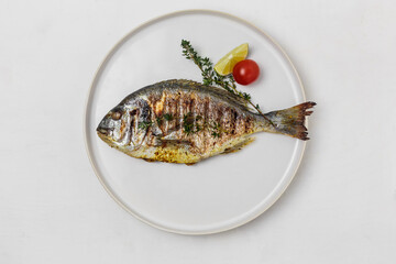 Grilled dorado with thyme, tomato, lemon and spices in a white plate on a white background