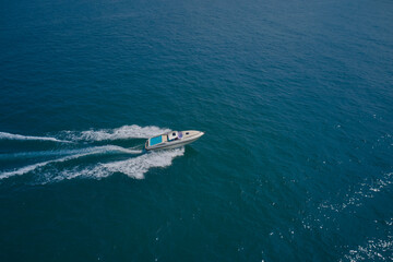 Aerial view luxury motor boat. Drone view of a yacht sailing across the blue clear waters. Top view of a white yacht sailing in the blue sea.