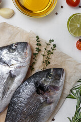Fresh fish dorado fish on cutting board on white table with ingredients for cooking