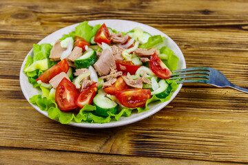 Tasty tuna salad with lettuce and fresh vegetables on wooden table