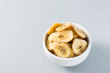 Baked banana chips in a white bowl on the table. Fast food. Copy space