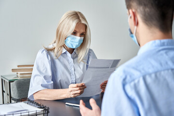 Female hr specialist manager, employer wearing face mask reading cv application of male candidate...