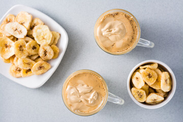 Quarantine  cuisine. Two cups with dalgona coffee and banana chips on a gray background. Top view