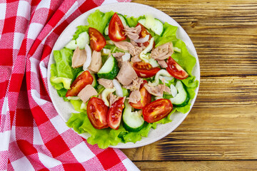 Tasty tuna salad with lettuce and fresh vegetables on wooden table. Top view
