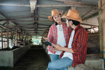 Girls and boys smile chatting wearing casual clothes and holding a digital tablet near a wooden fence with a cow farm stable in the background