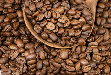 Grains of coffee in a wooden spoon on a wooden background.