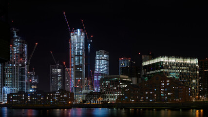Nighttime view over River Thames to American embassy residential apartments and new building construction and cranes with red lights