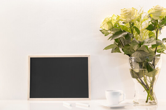 Modèle de tableau noir en ardoise avec espace vide pour logos, inscription publicitaire. Cadre en mode paysage sur un espace de travail avec des roses et des craies.	